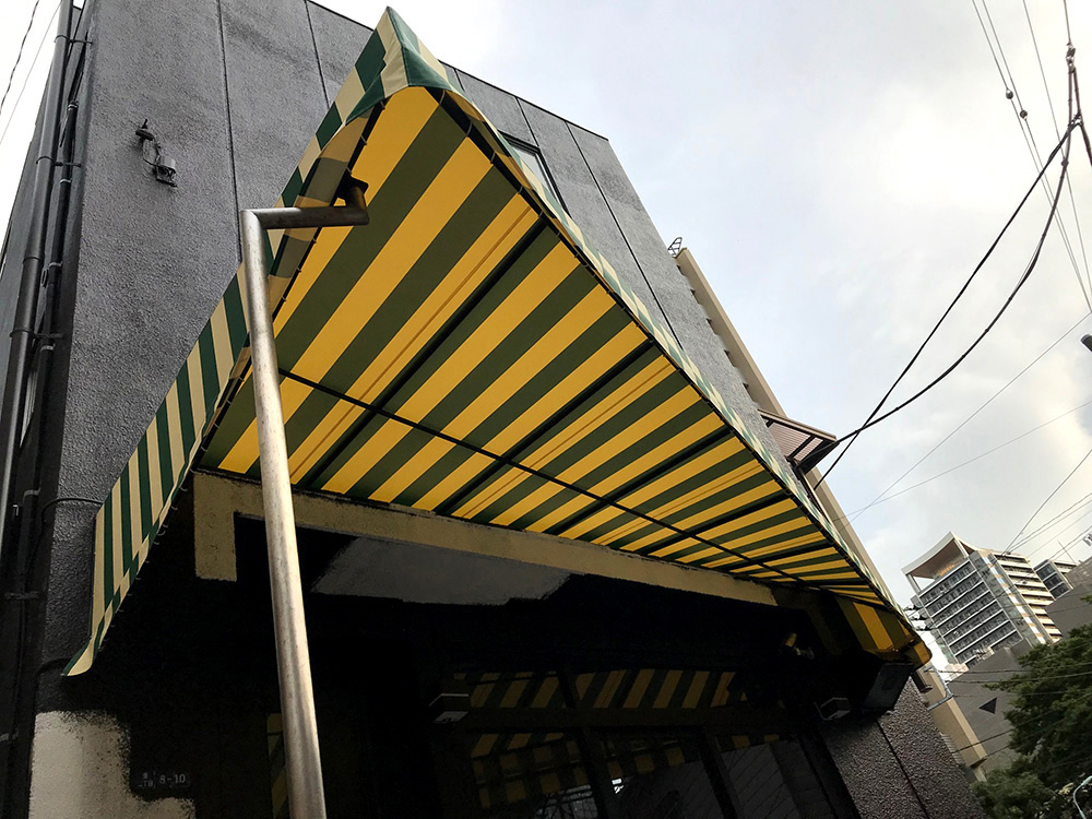 画像：店舗軒先に設置された変形型BOXテントの生地張替え工事